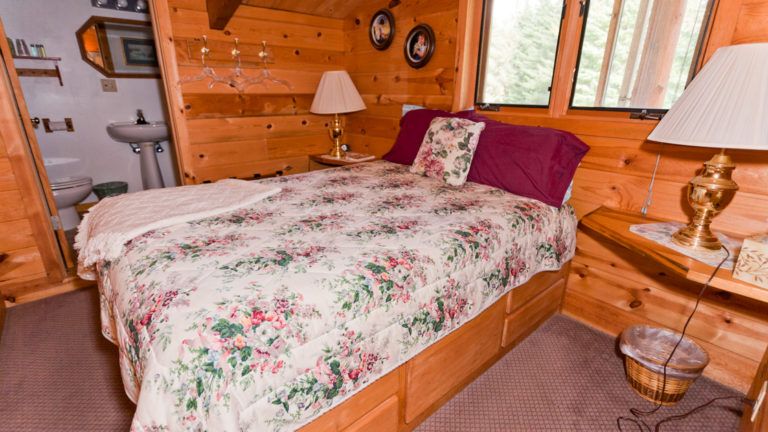 Room at Annie Mae Lodge with wood walls and white queen bed with a view of the bathroom through the door.