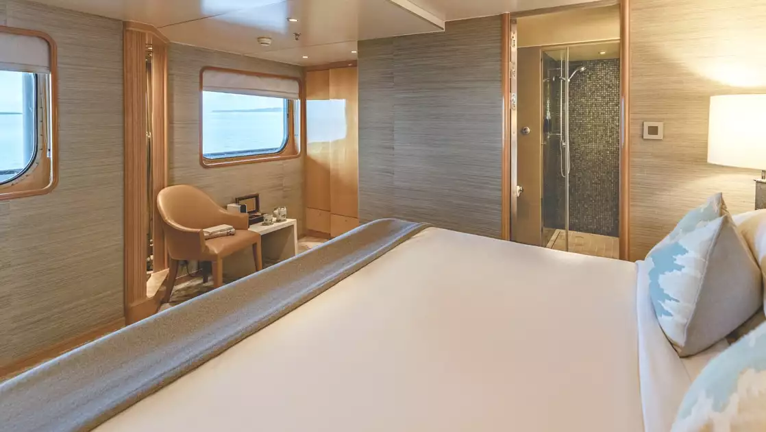 double bed in Aqua Blu ship cabin with wooden accents, view windows & gray textured walls.