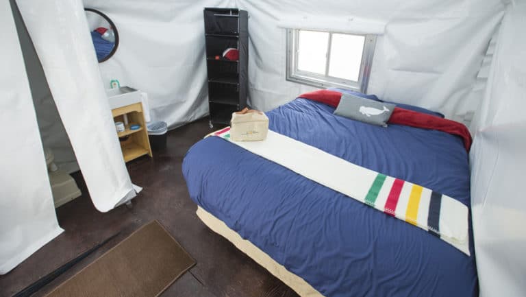 Arctic Watch room in a large white tent with large bed, coat rack, hanging shelves and window.