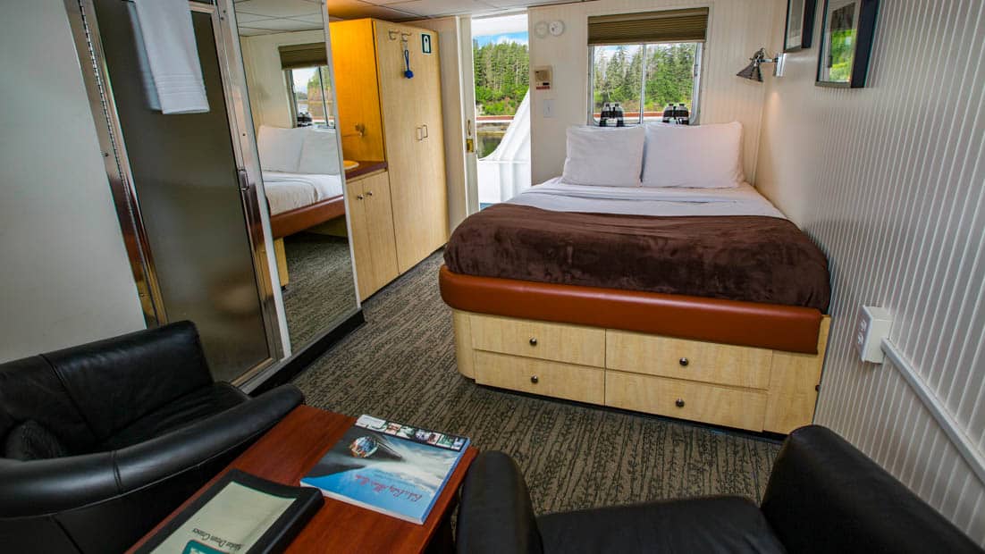 Deluxe stateroom aboard Baranof Dream with bed, two chairs, and window.