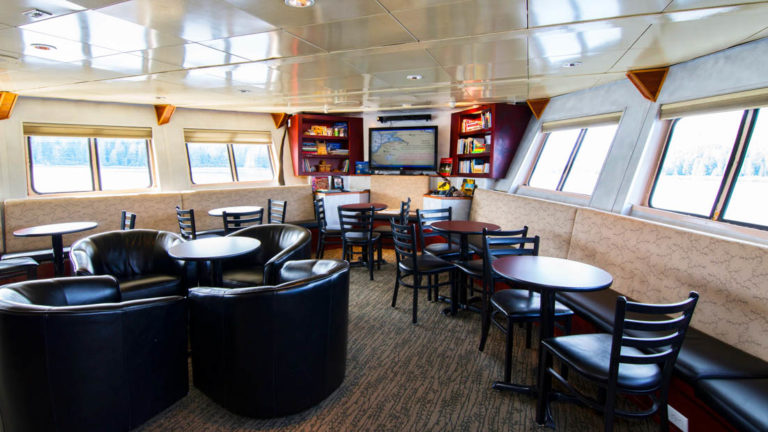Lounge are with chairds, tables, tv, and windows aboard Baranof Dream.