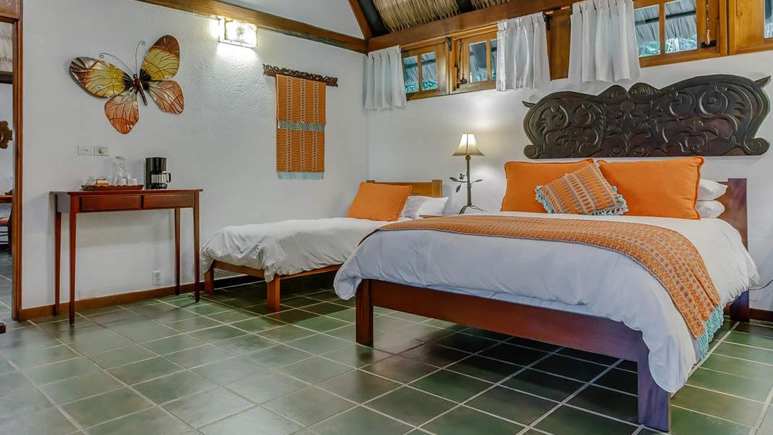 Large bed and nearby daybed with tapestries and local woodworking decorating the walls of a garden suite at Chaa Creek Lodge in Belize