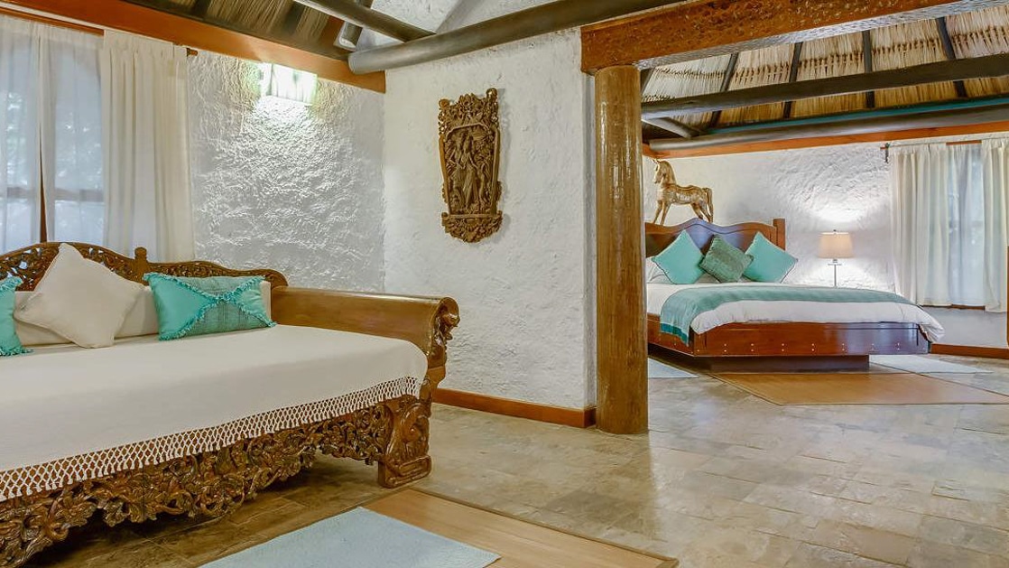Wood daybed in living room with master bedroom visible in the Macal River Suite at Chaa Creek Lodge in Belize.