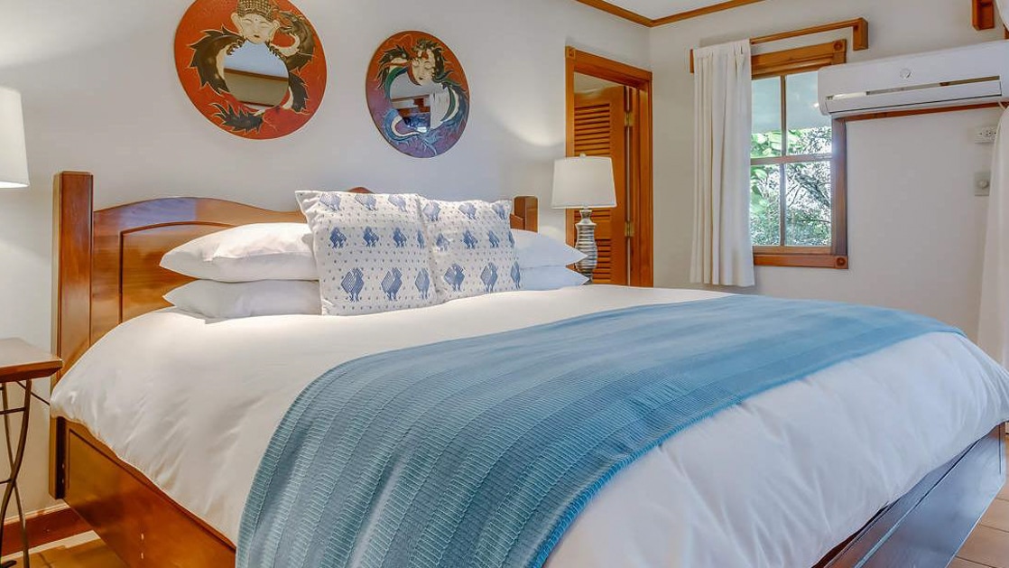 King bed with fresh blue decor and local wood artwork in the spa villa master bedroom at the Lodge at Chaa Creek in Belize.