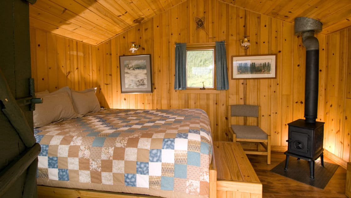A queen-sized bed and a wood stove keep guests cozy and warm while staying at Camp Denali, a wilderness lodge with historic ties to the preservation of the national park in Alaska.