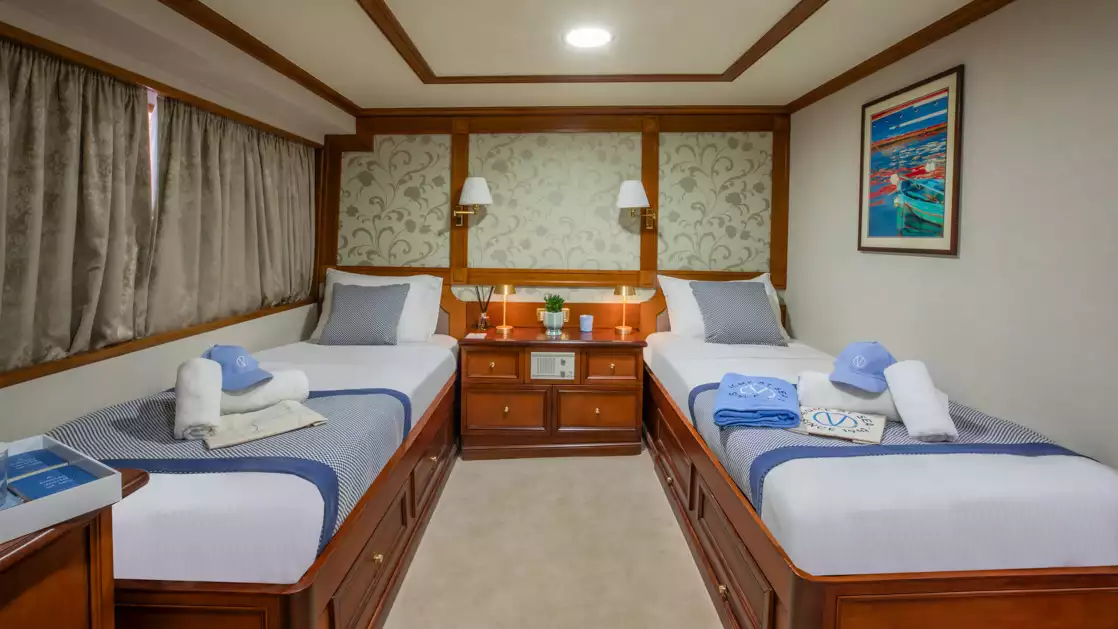 Category A cabin aboard Callisto yacht showing two twin beds with a window and a basket sitting on one bed