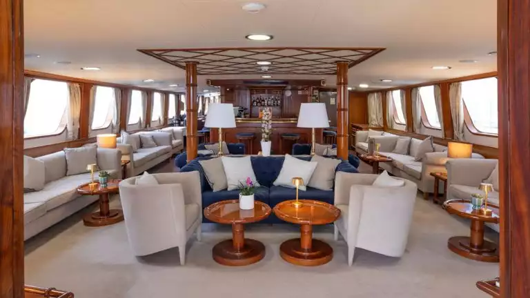 indoor of small cruise ship with tan carpets and modern furniture, large windows on both sides with wood accents