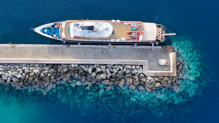 Aerial drone view of the Callisto Mediterranean yacht at a dock with clear water and jetty rocks