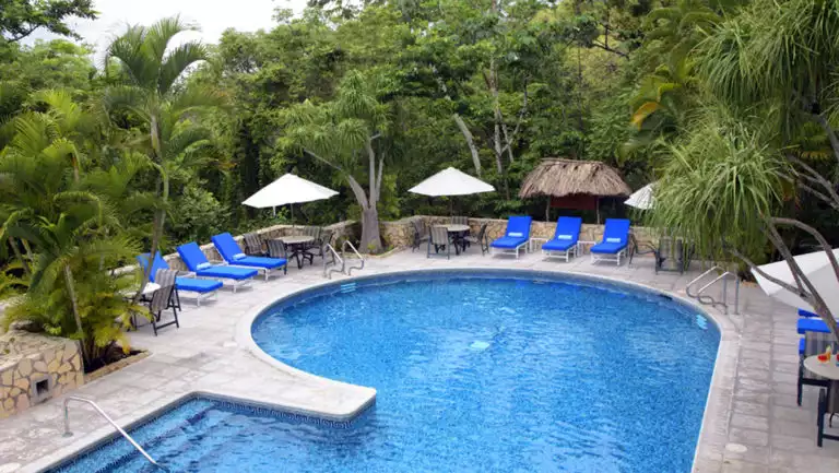 large pool surrounded by pool chairs and tall green trees at Camino Real Tikal Hotel.