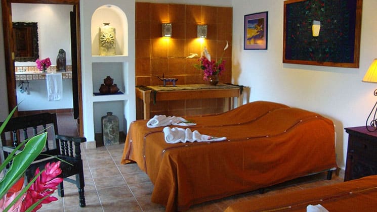 room in the candelaria lodge in guatemala with two beds, pictures on the wall and a doorway leading to another room