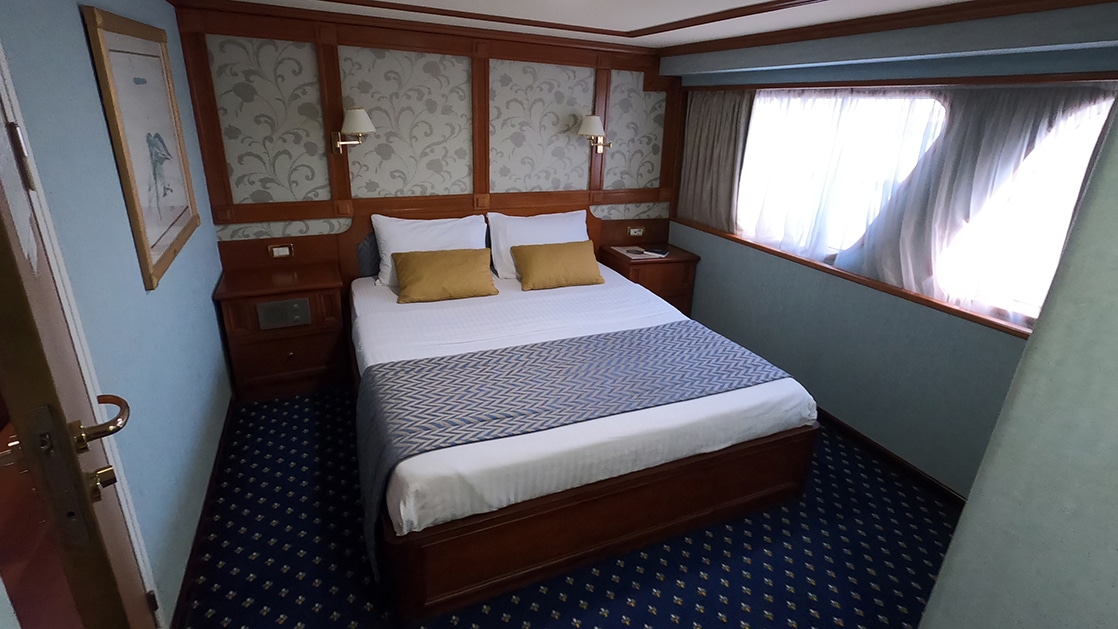 Category P cabin aboard Callisto yacht showing a double bed in the center of the cabin with a window to the right