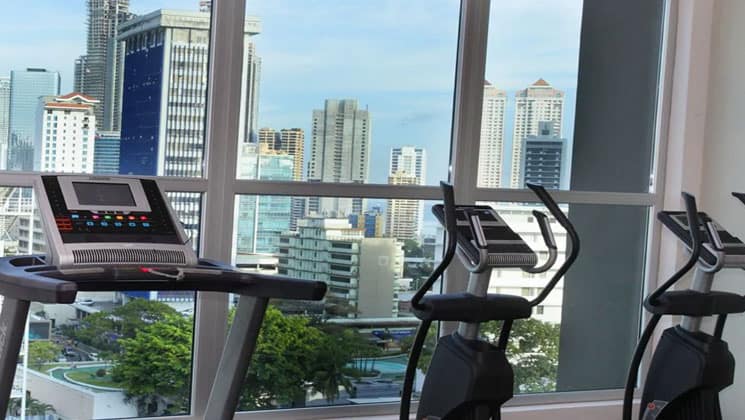 gym room of the clarion victoria panama hotel with treadmills in front of large windows looking out at the city's skyscrapers