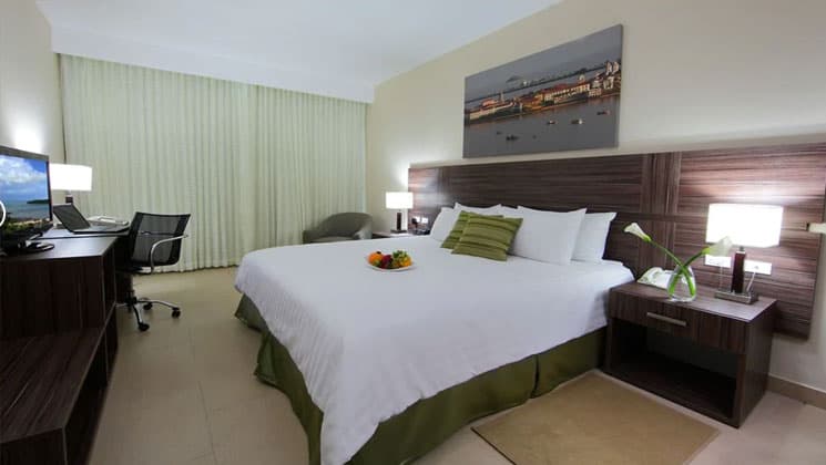 room with a king bed with green accents and a picture on the wall at the clarion victoria panama hotel