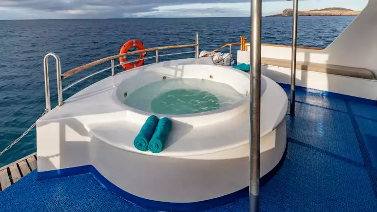Empty white Jacuzzi tub with 2 rolled turquoise towels on Corals Galapagos yachts with blue mats on aft of ships.
