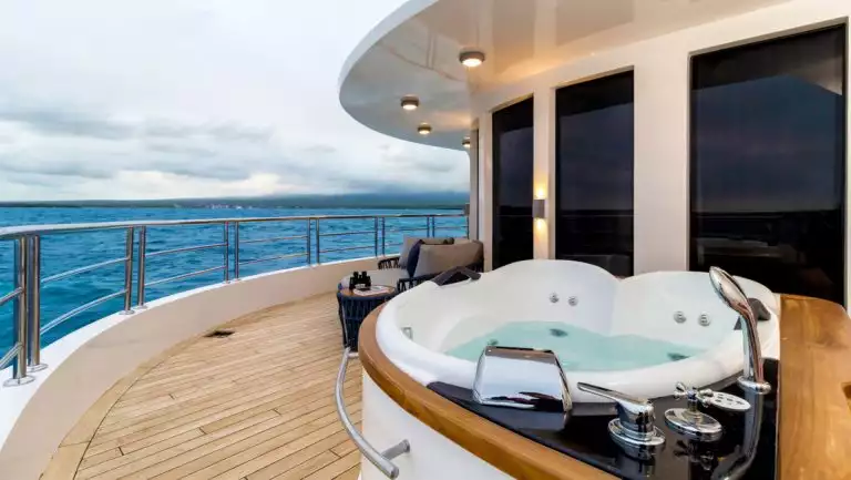 2-person Jacuzzi sits on teak wraparound deck with padded loveseat & side table by floor-to-ceiling windows on Cormorant II.
