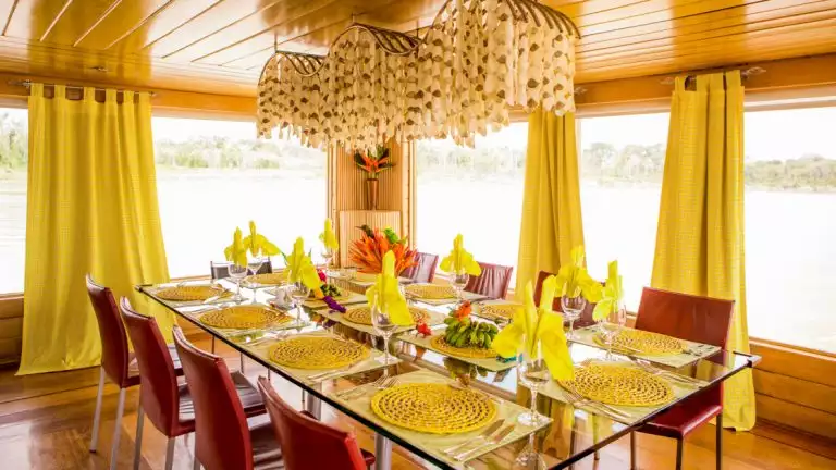A beautiful dinning room with bright yellow accents and warm honey colored woods with a pretty chandeller Delfin I Amazon River Cruise in Peru