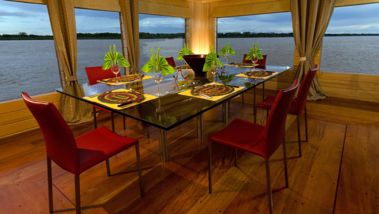 Glass dining table with seating for six near large picture windows in dining room aboard Delfin I on the Amazon River