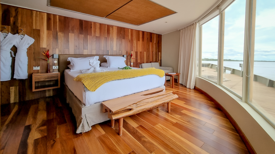Large expansive windows with beautiful wood finishes featuring robes and a flower on a night stand aboard the Delfin III Amazon