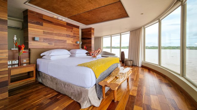 Beautiful wood finishes large wrap around windows featuring large bed chase lounge aboard Delfin III on the Amazon in Peru