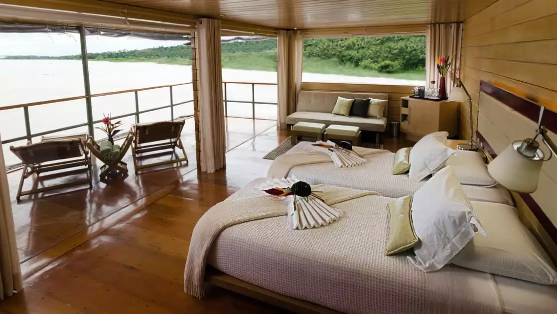 Master Suite with two beds, couch and private balcony with lounge chairs aboard Delfin I on the Amazon River