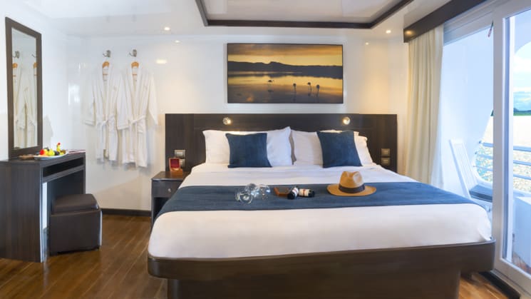 Suite with large bed, bedside table, vanity and private balcony aboard Cormorant catamaran in the Galapagos Islands