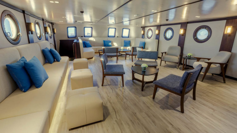 Lounge area on the Evolution with banquette seating, chairs and small tables with portholes.