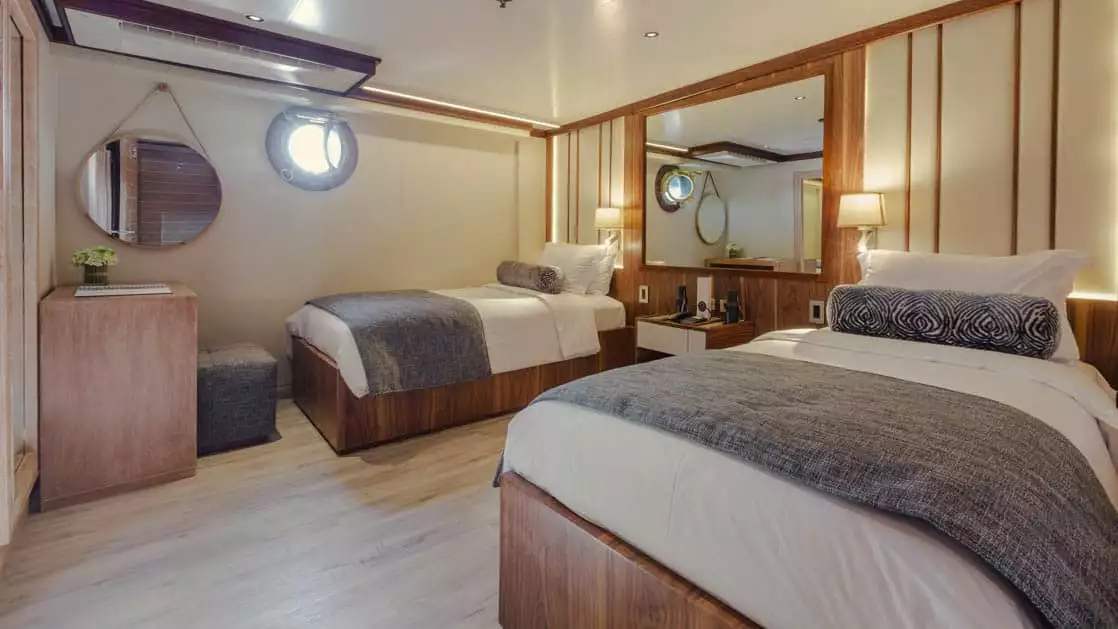 Evolution Premium Stateroom with twin beds, nightstand, desk and porthole.