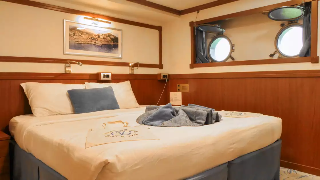 A large comfortable double bed with two portholes blue accent aboard the Galileo while cruising the Aegean sea Mediterranean