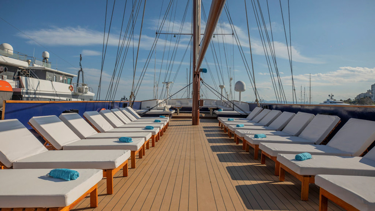 Big open sun deck with rows of plush white chaise loungers below the rigging & blue sky on the Galileo cruise ship.