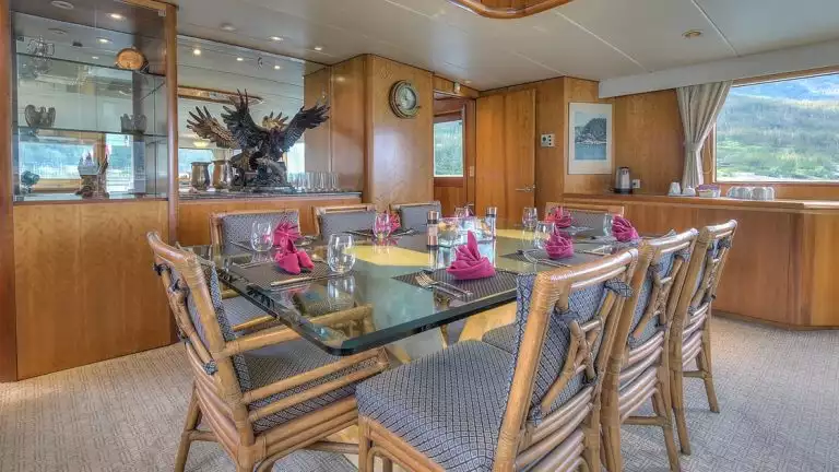 Glass table set for dinner with 8 chairs around it in the middle of the dinning room aboard the Golden Eagle yacht.