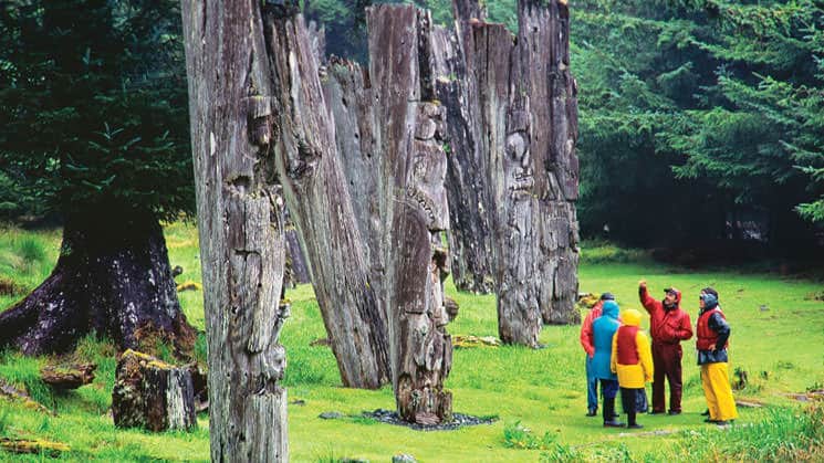 Small ship cruise passengers with their guide in the forest in Haida Gwaii, British Columbia looking at old totems