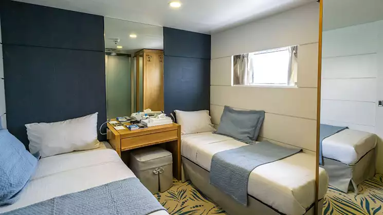 Harmony G yacht Category A stateroom with 2 twin beds, a window, a mirror and blue and white bedding