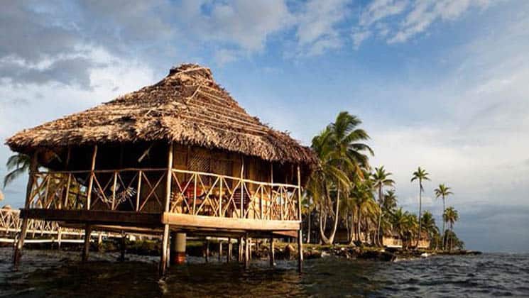 A thatched-roof cabana on a platform above the water and adjacent to a grove of palm trees, the Yandup Lodge in the San Blas islands in Panama is paradise