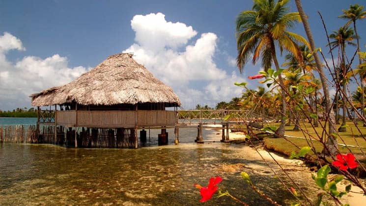A side view of a cabana with a thatch-roof, built on a platform above the water, is connected to the island. The idyllic eco Hotel Yandup in San Blas, Panama, is a slice of paradise