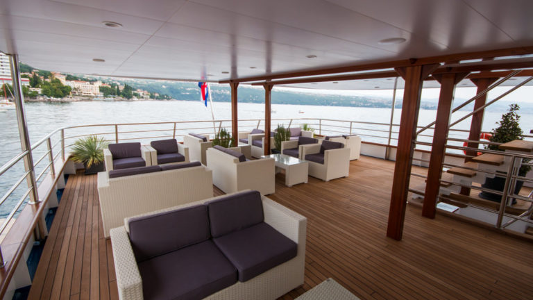 Outdoor sundeck with couches, chairs, coffee tables and stairwell at the stern of the Infinity.