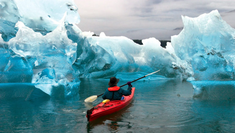 Kayaker paddling through a uniquely sculpted ice berg in tracy arm fjord, Alaska