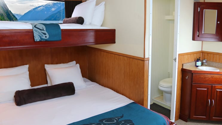 Queen bed with single berth above it, small window, sink, mirror and shoilet, on the Kruzof Explorer Alaska small ship.