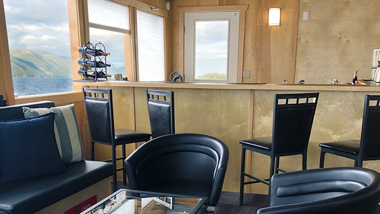 Light-wood bar, view windows & black leather couch & chairs, on the Kruzof Explorer Alaska small ship.