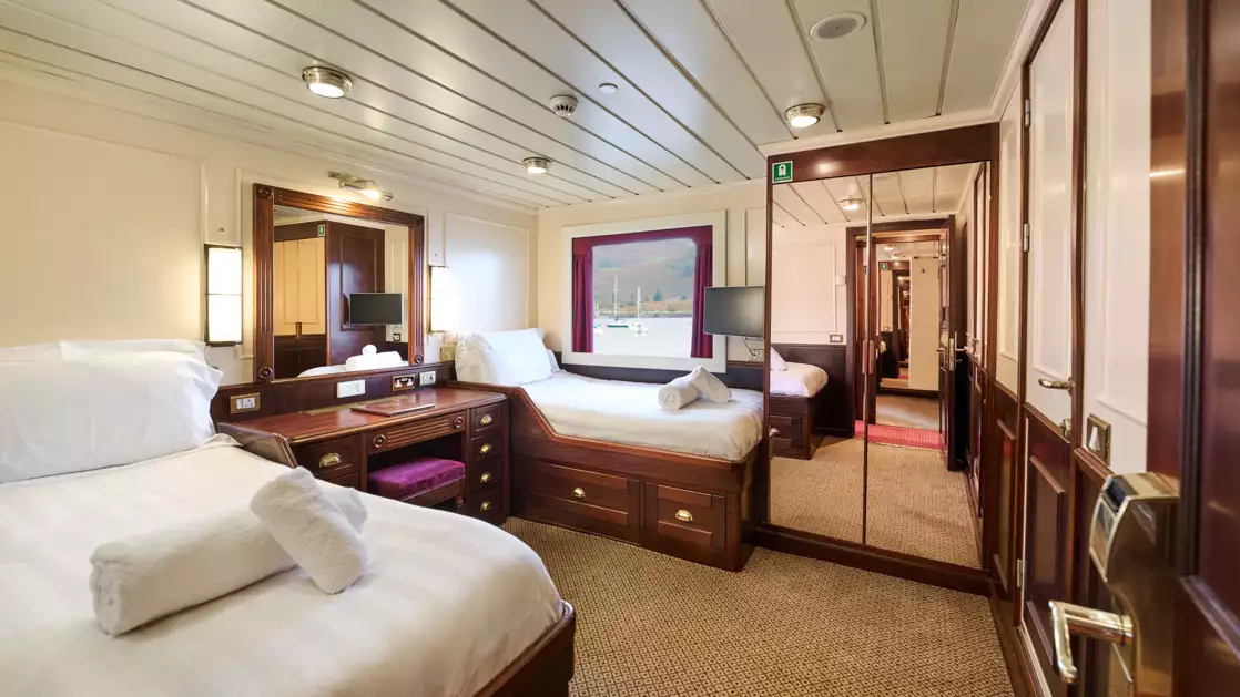 bedroom aboard small cruise ship, with two beds with folded towels and a picture window.