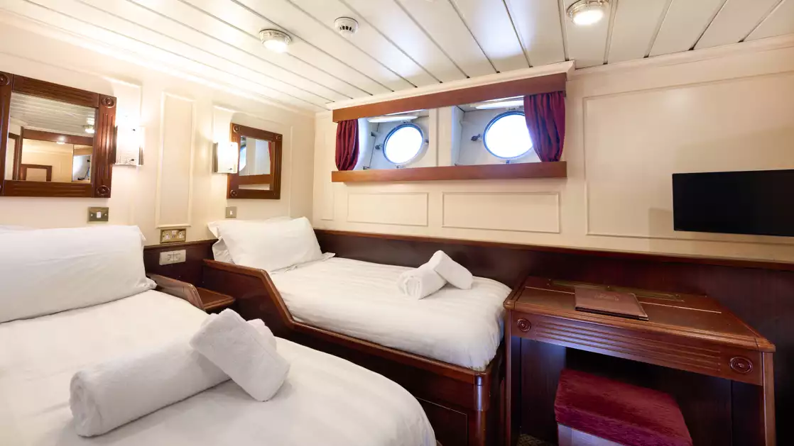 Two twin beds aboard small ship with folded towel and port windows.