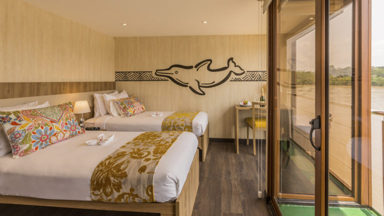 Deluxe Twin aboard Manatee Amazon Explorer with floor to ceiling windows, sliding glass door out to private balcony, nightstand and reading lights.