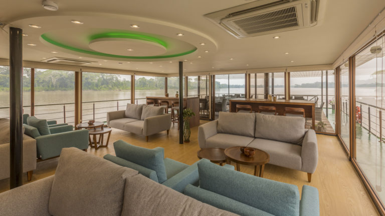 Manatee Amazon Explorer lounge with couches, tables, bar and floor to ceiling windows.