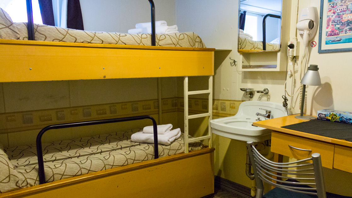 A bunk bed with a large featured window a desk and sink with a blow dryer aboard the Ushuaia which sails around the Antarctic
