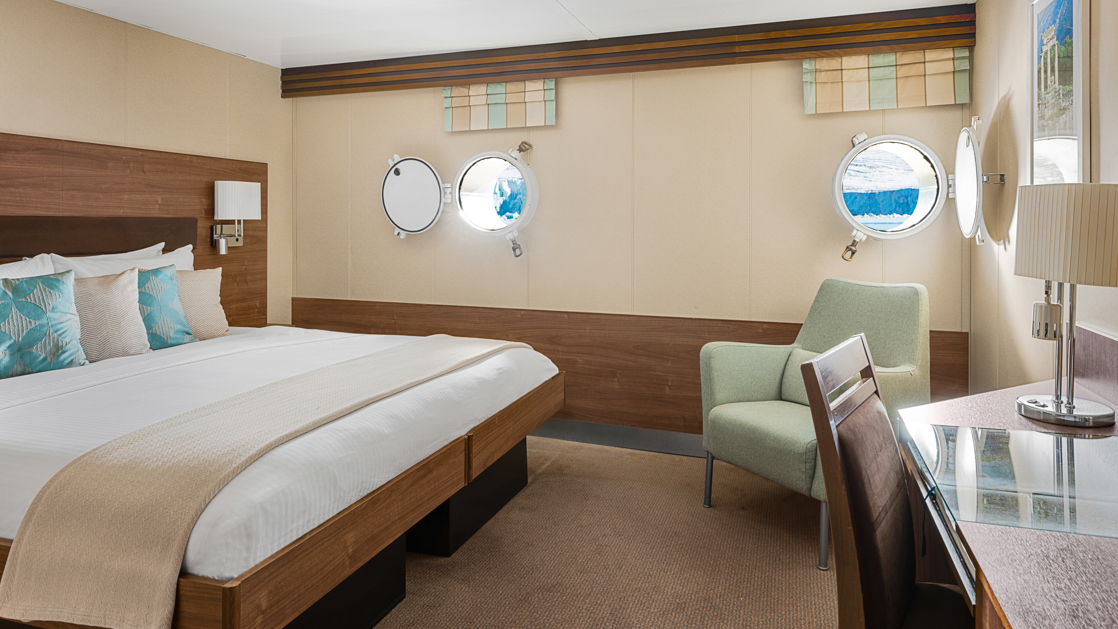 A large double bed and portholes are featured in this category 1 cabin with warm wood aboard the National Geographic Explorer