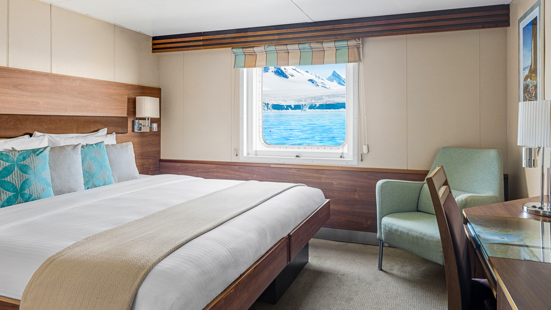 A large double bed and window are featured in this category 2 cabin with warm wood aboard the National Geographic Explorer
