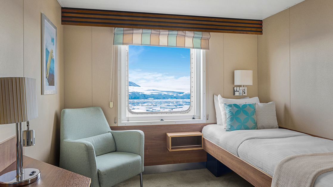 Category B Solo cabin with bed, nightstand, desk, chair and large window aboard National Geographic Explorer polar expedition ship