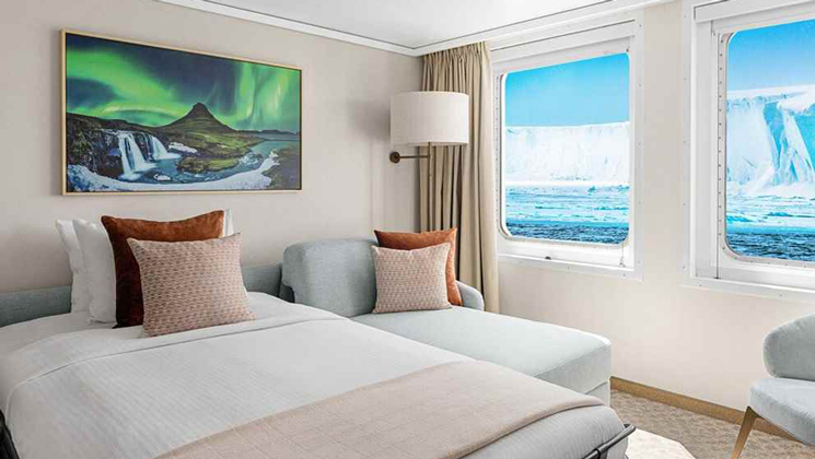 Rendering of Category 6 Suite on Nat Geo Explorer ship with double bed, chaise lounge chair, light colors & window onto ice & snow.