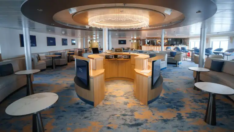 Interior lounge on National Geographic Explorer ship with round dais under chandelier, surrounded by padded benches & small tables.
