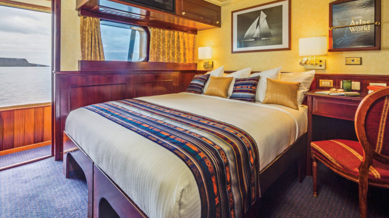 Large bed, desk, chair, window and door to outside cabin aboard National Geographic Islander expedition ship in Galapagos Islands