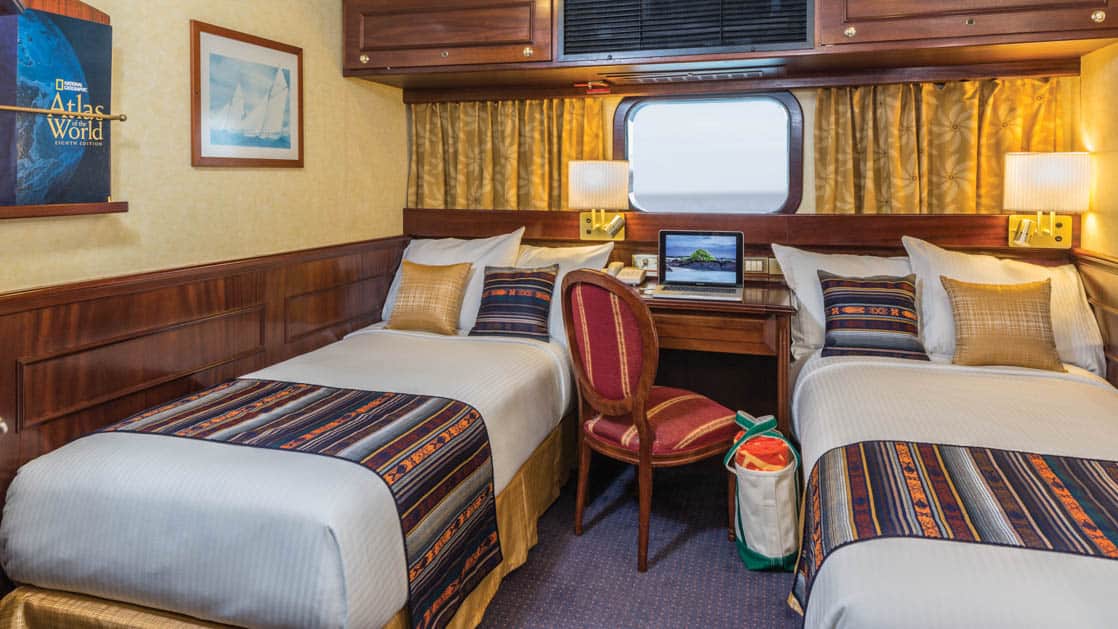 Two beds, desk, chair and window in cabin aboard National Geographic Islander expedition ship in Galapagos Islands